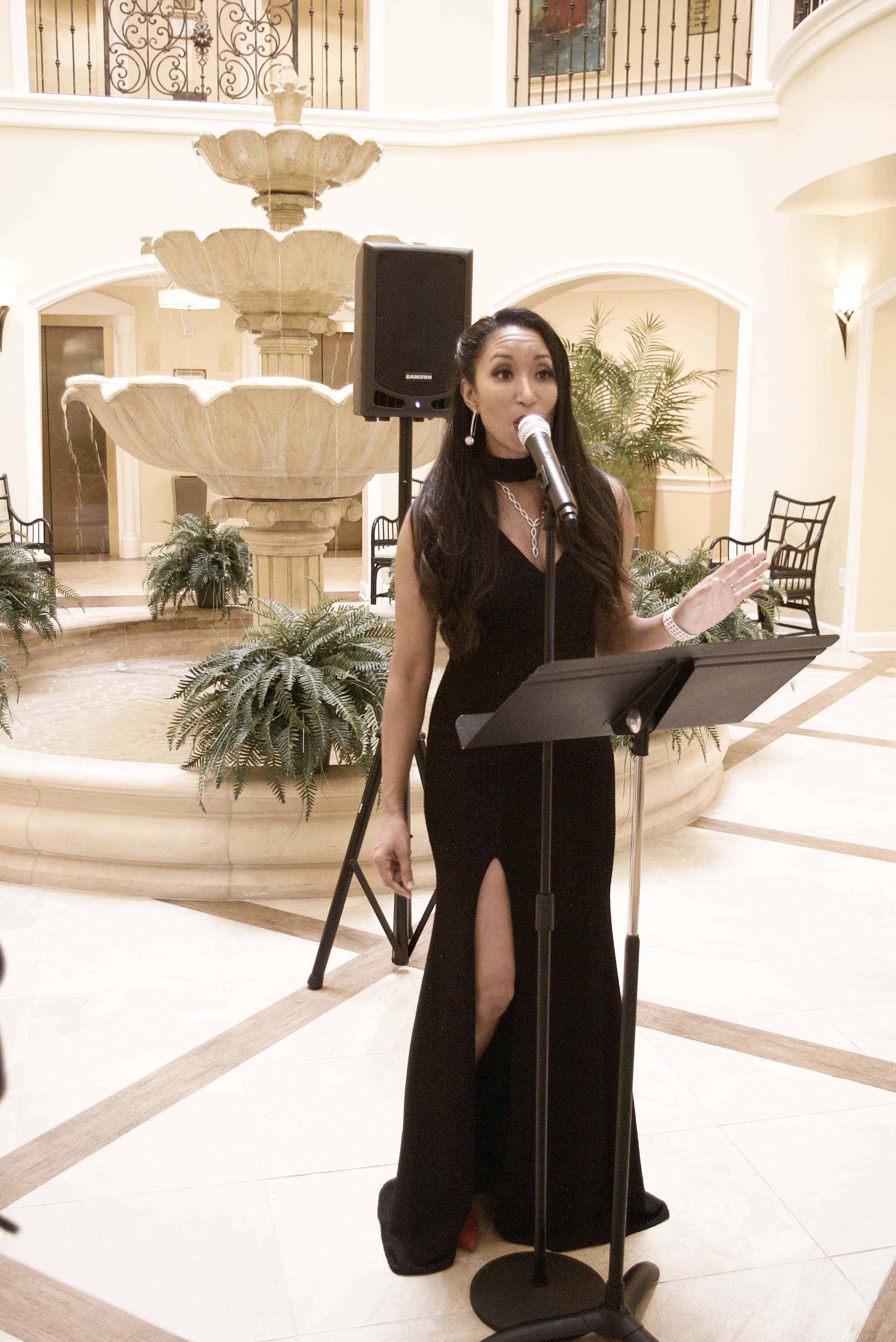 Deanna singing by a fountain into a microphone in a black dress.