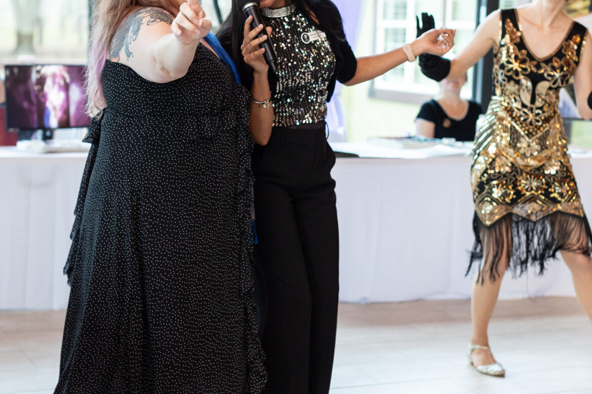 Deanna singing at an event, getting a woman involved in singing with a flapper dancer behind her.