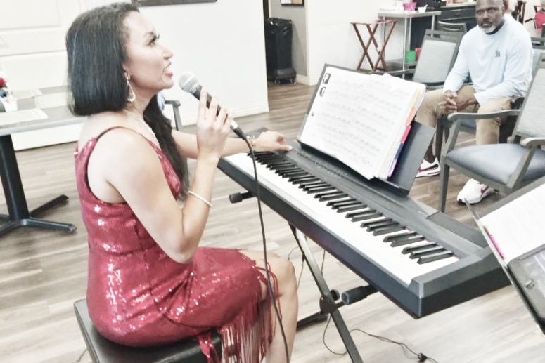 Deanna sitting at a keyboard talking to the audience at a senior living facility