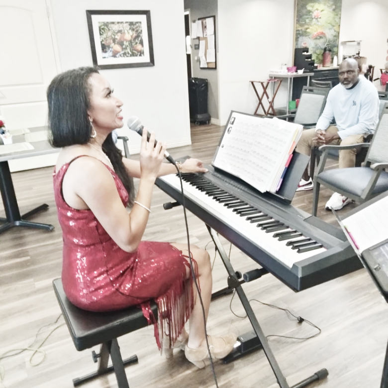 Deanna sitting at a keyboard talking to the audience at a senior living facility