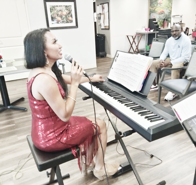 Deanna sitting at a keyboard talking to the audience at a senior living facility