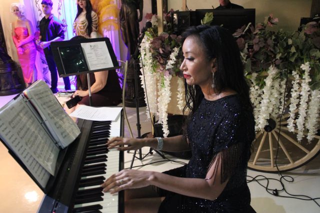 Deanna L. Giron playing piano with sheet music at a floral-draped event